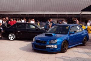 A vibrant car show featuring a blue Subaru Impreza and black Mitsubishi Lancer.