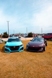 Two stylish cars showcased at a sunny outdoor car exhibition on grass field.